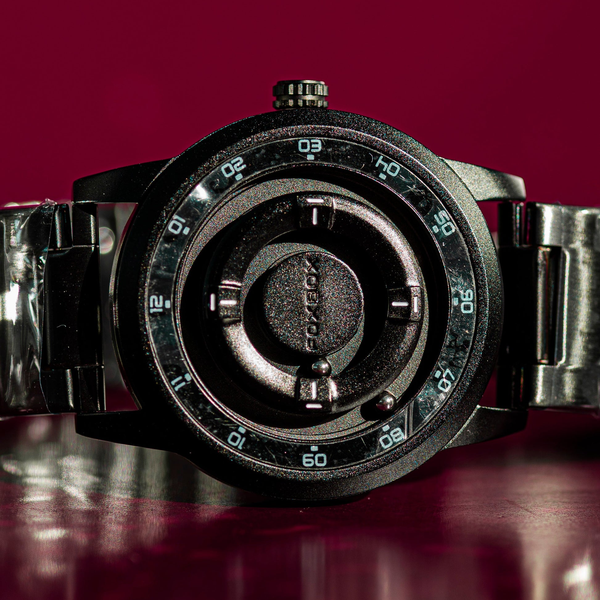 Black wristwatch with metallic band on a reflective surface with a purple gradient background