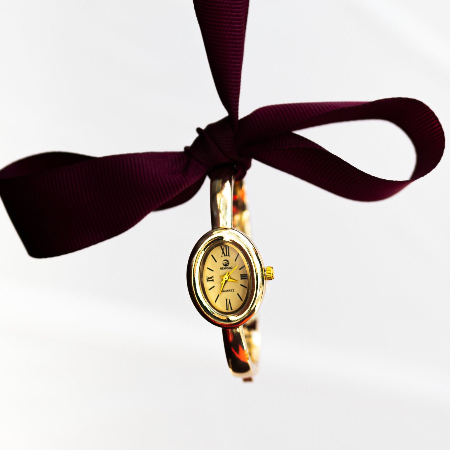 Gold watch on a purple ribbon against a white background