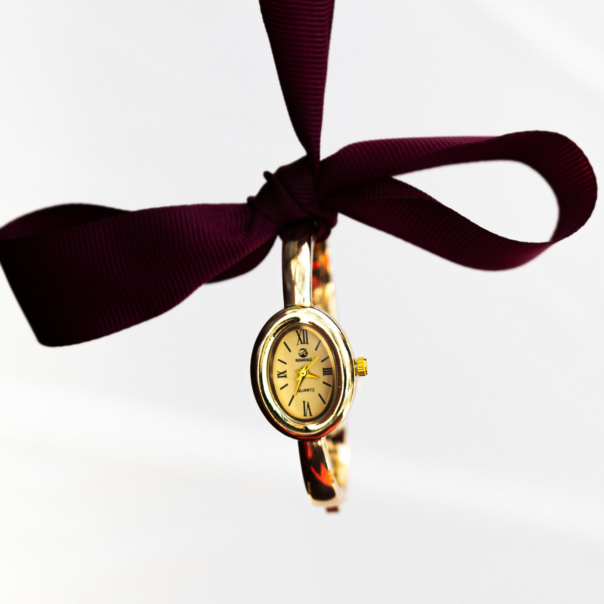 Gold watch on a purple ribbon against a white background