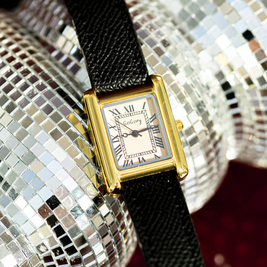 Gold watch with a black strap on a reflective silver background