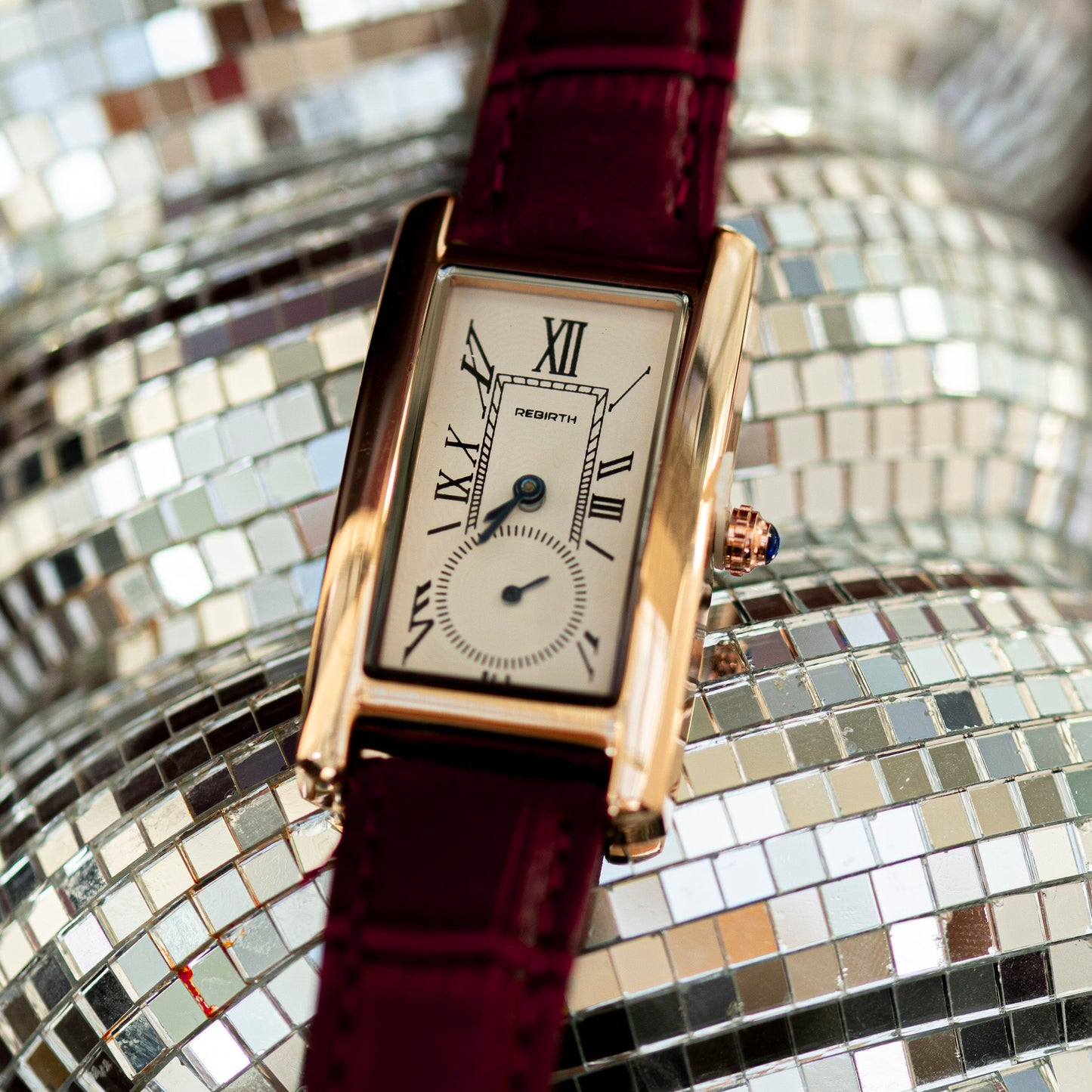 Gold watch with a burgundy strap on a disco ball background