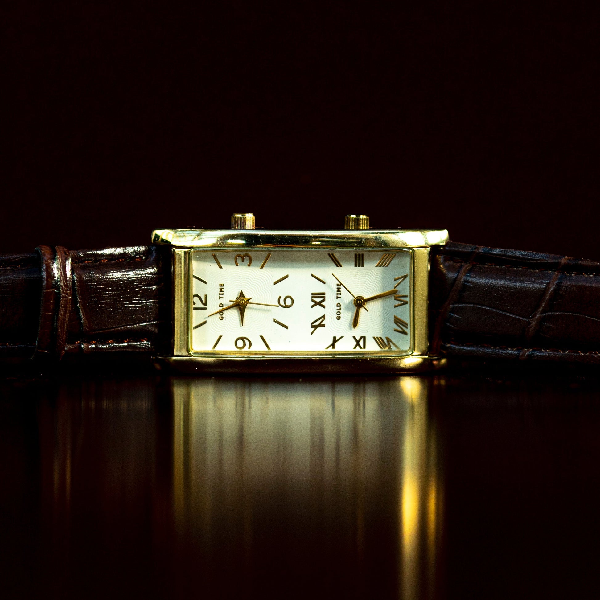 Gold wristwatch with a brown leather strap on a reflective surface with a dark background