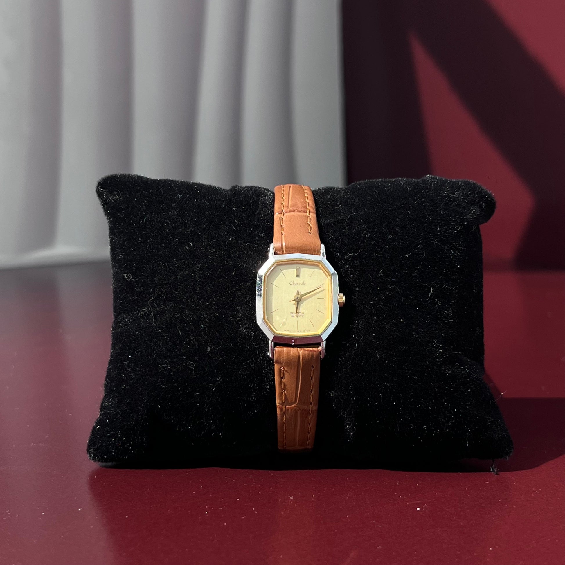 Wristwatch with brown strap on a black cushion against a red background