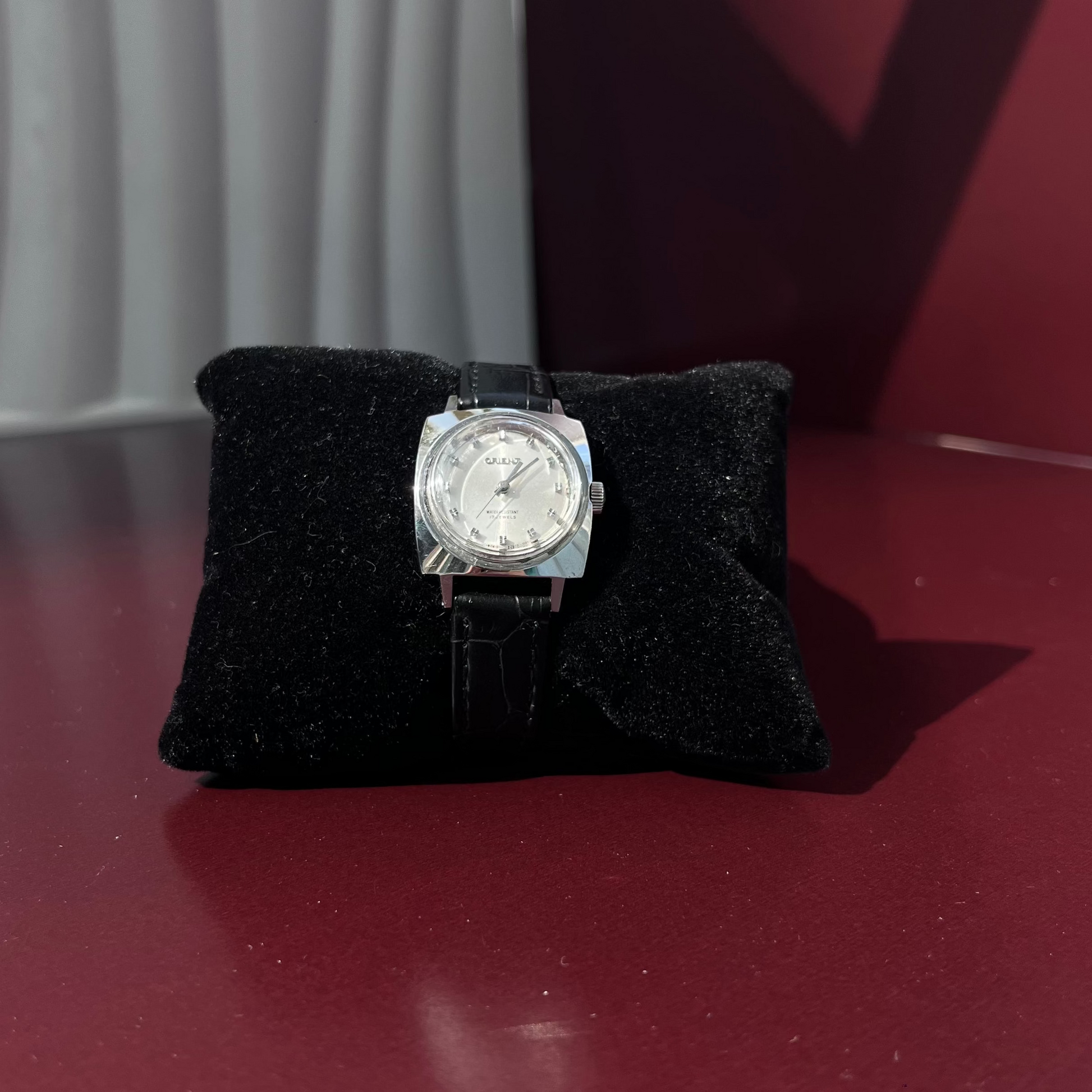 Silver watch on a black cushion against a red background