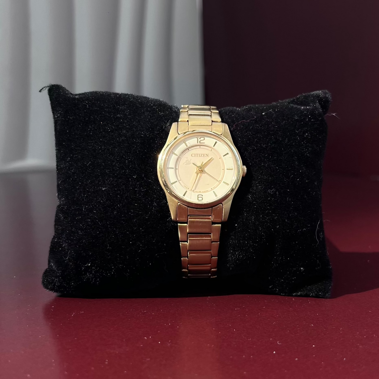Gold wristwatch on a black cushion against a red background