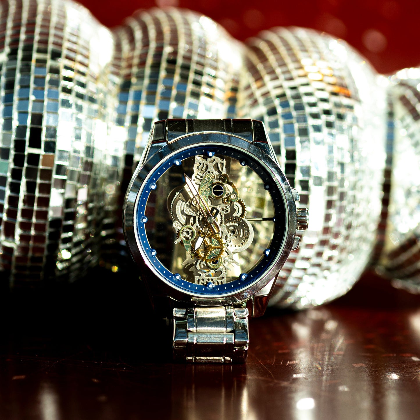Luxury watch with intricate design in front of disco balls on a reflective surface
