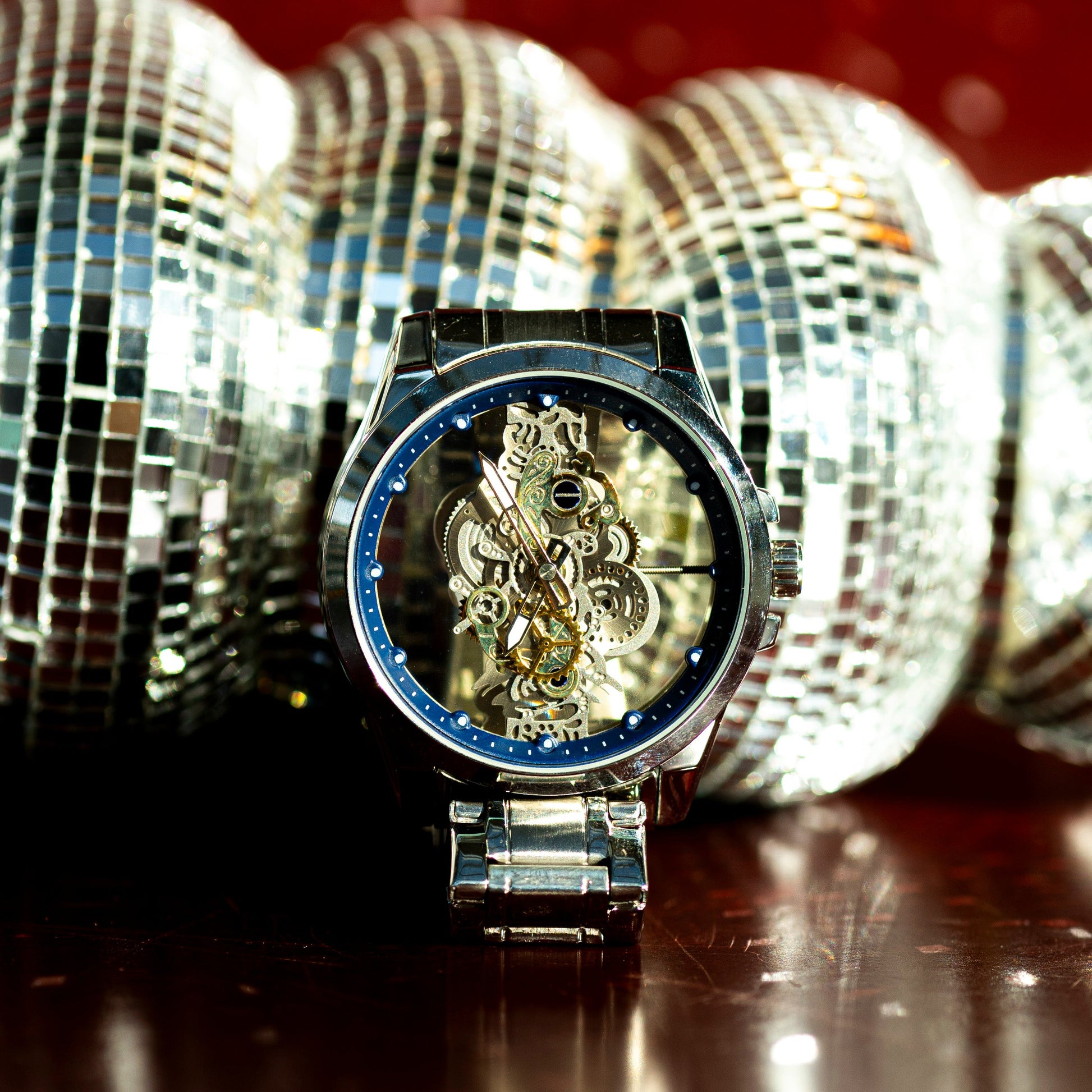Luxury watch with intricate design in front of disco balls on a reflective surface