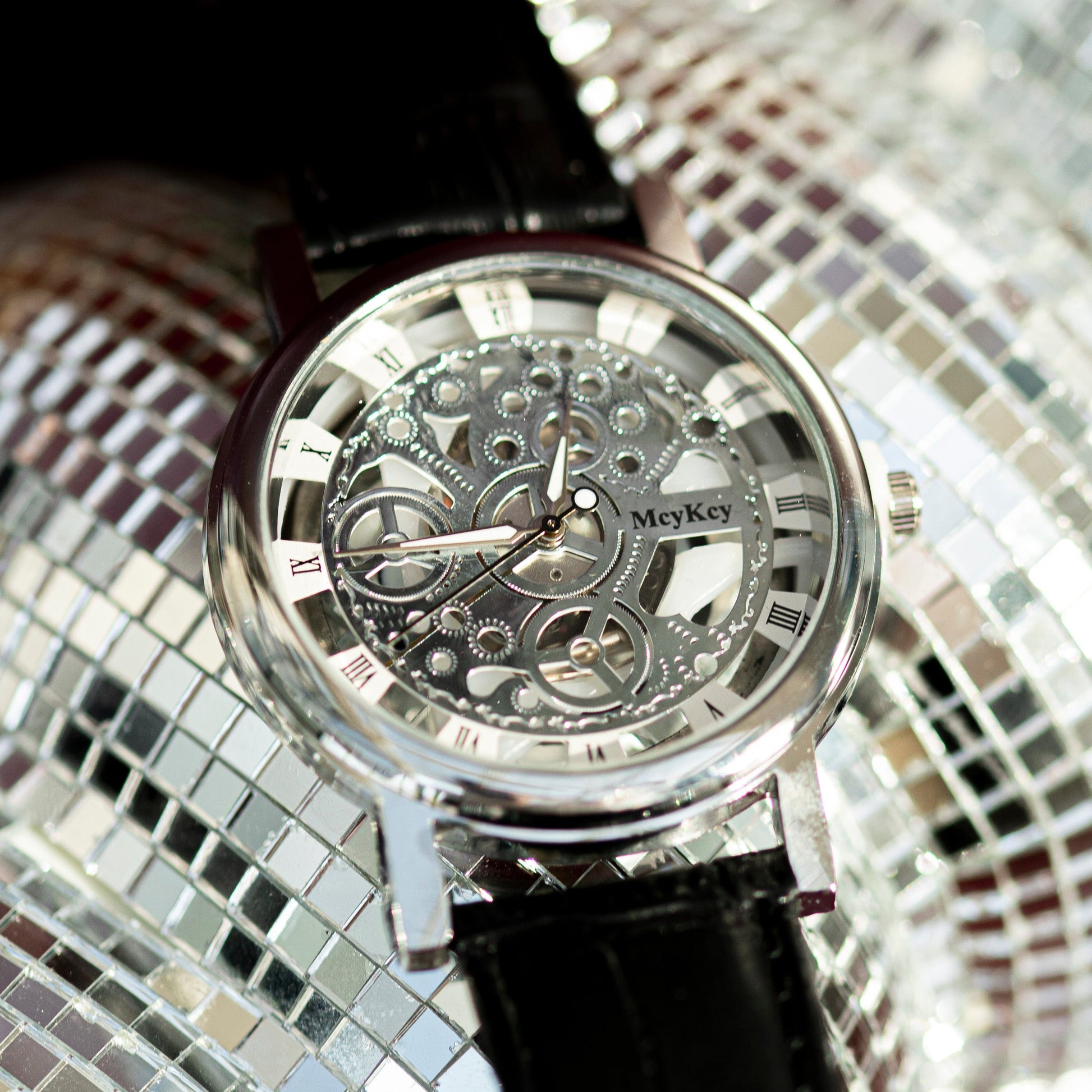 Mechanical watch with black strap on a reflective surface