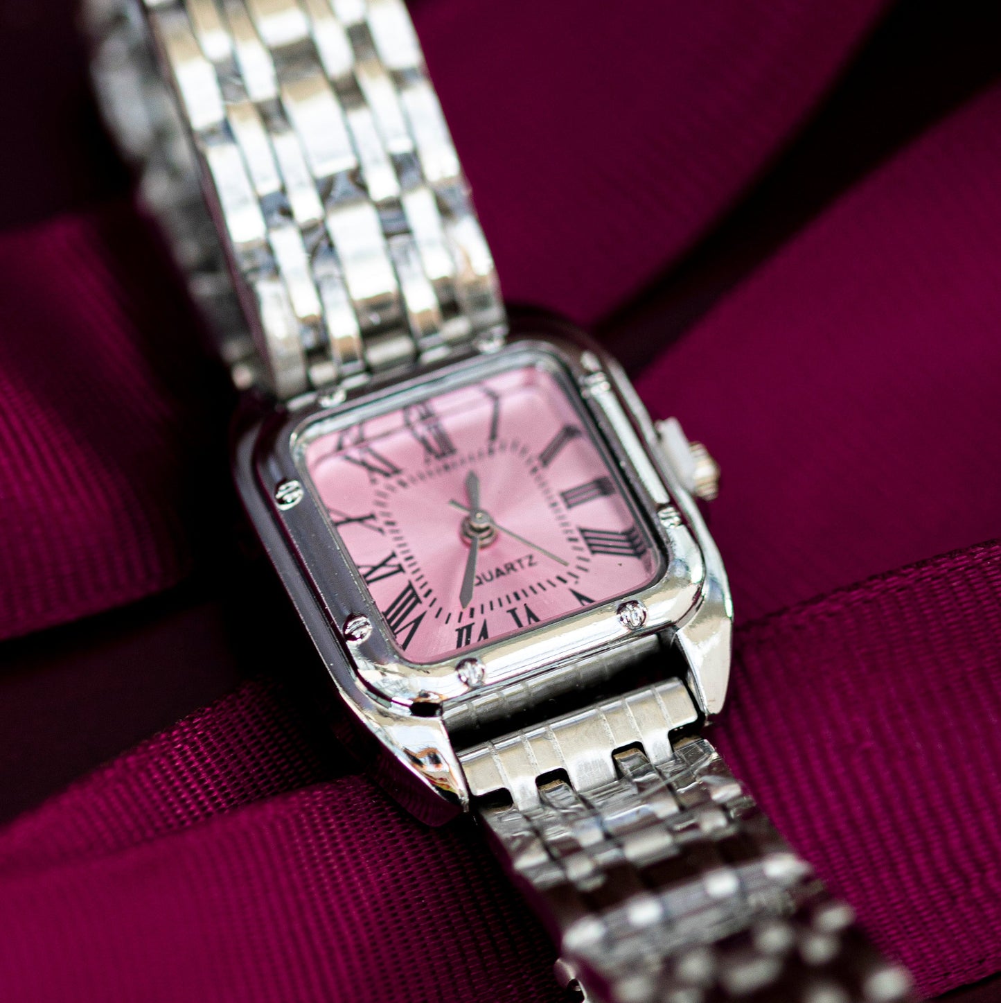 Silver watch with a pink face on a purple ribbon