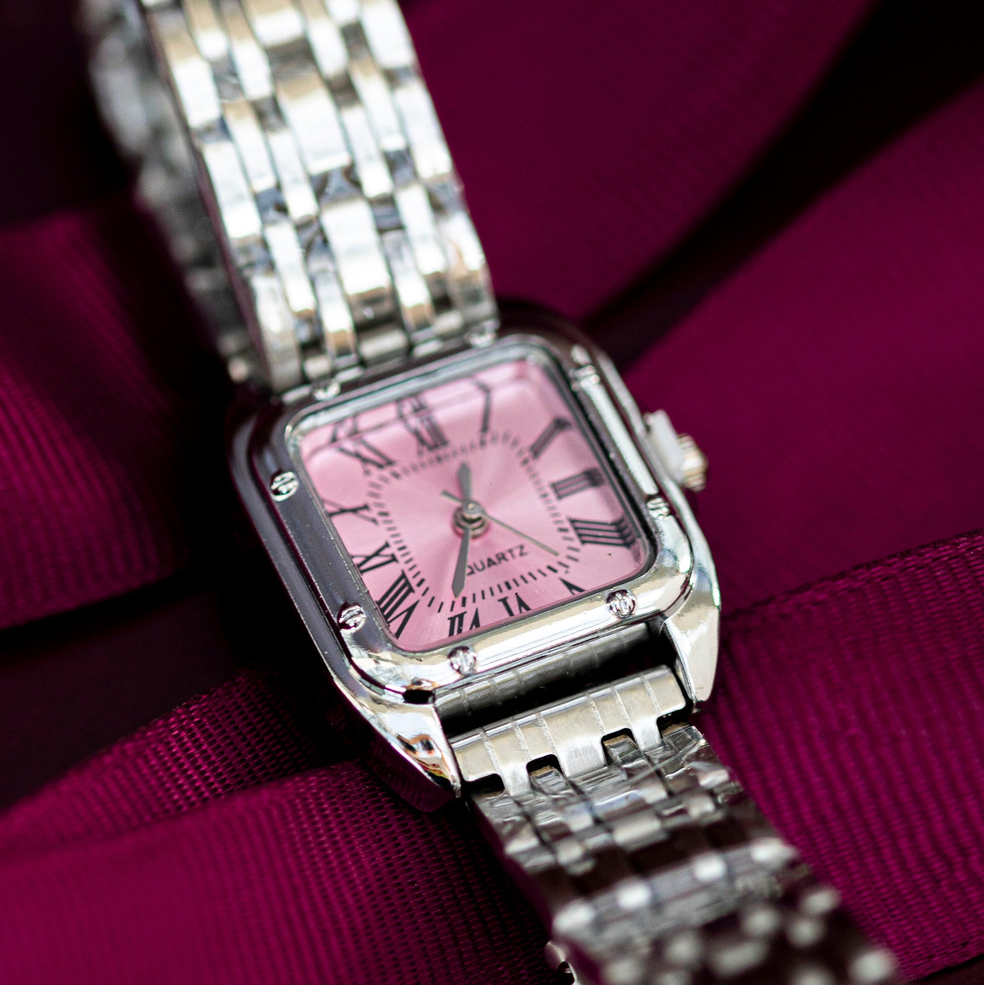 Silver watch with a pink face on a purple ribbon