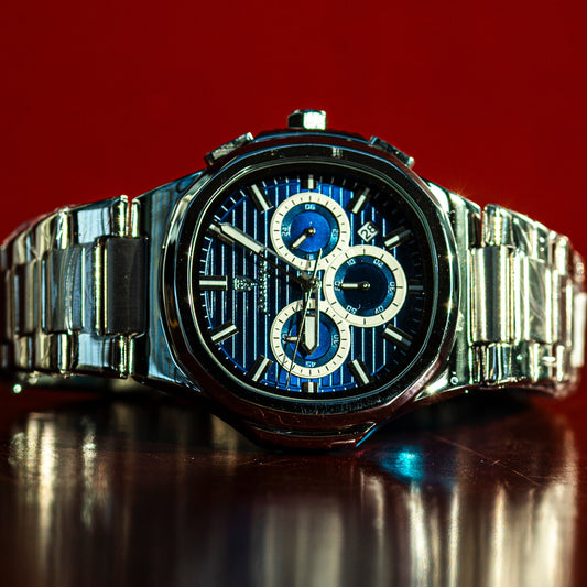 Silver watch with a blue face on a reflective surface against a red background