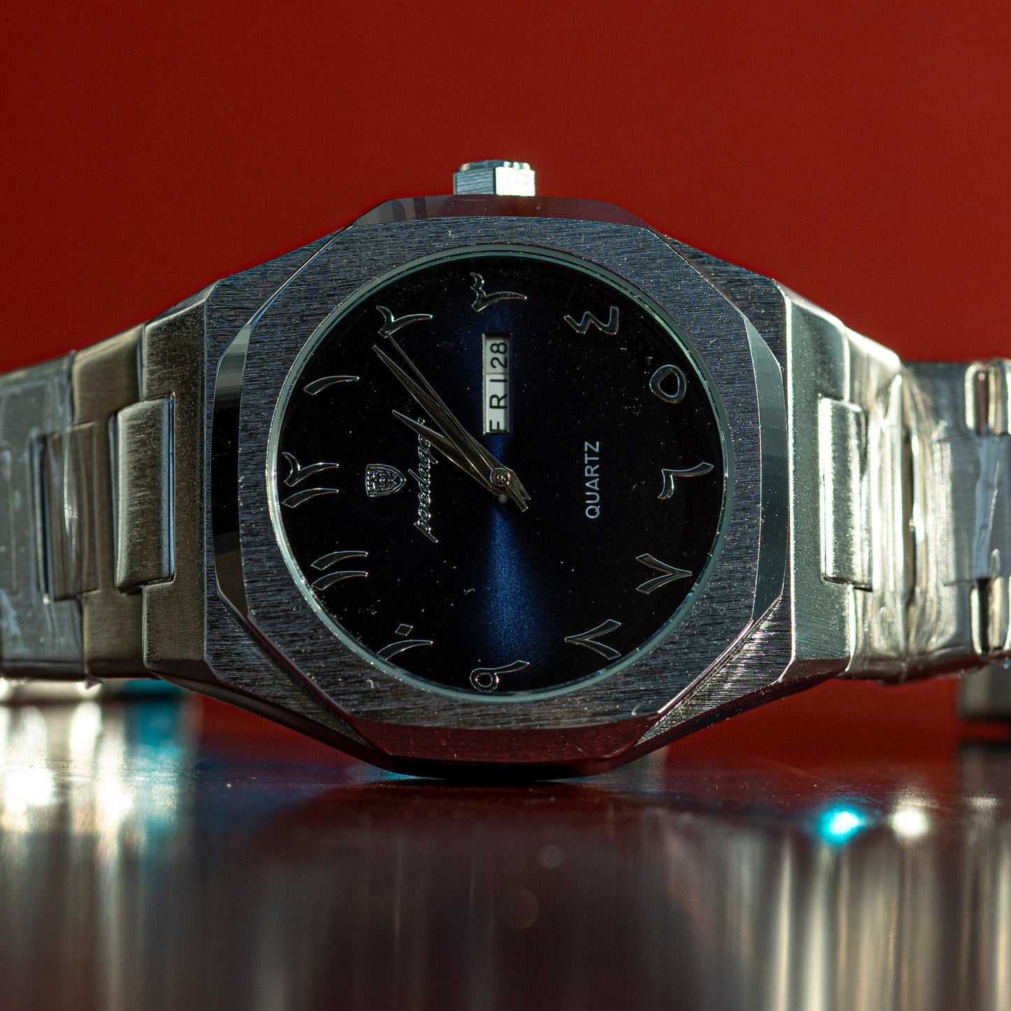 Silver watch with black face on a reflective surface against a red background