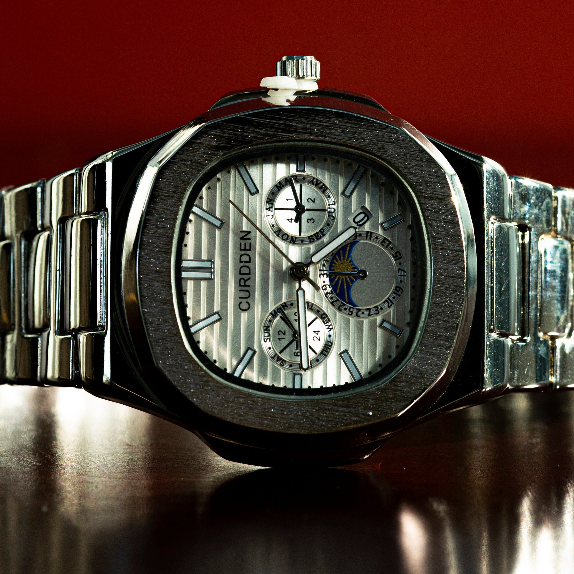 Silver watch with detailed face on a reflective surface against a red background