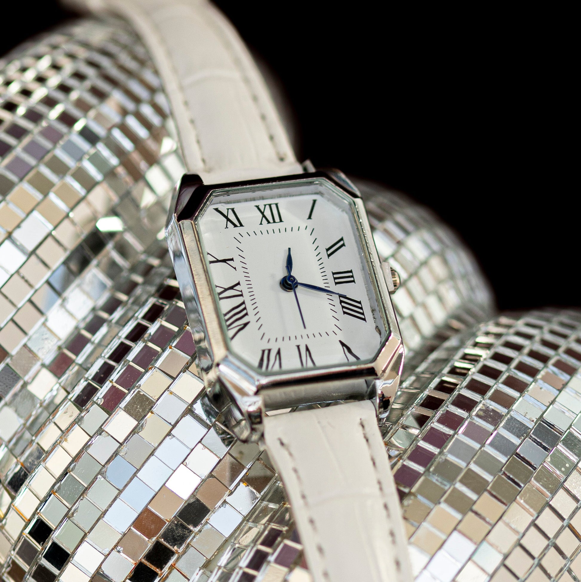 Silver watch with white face and leather strap on a disco ball