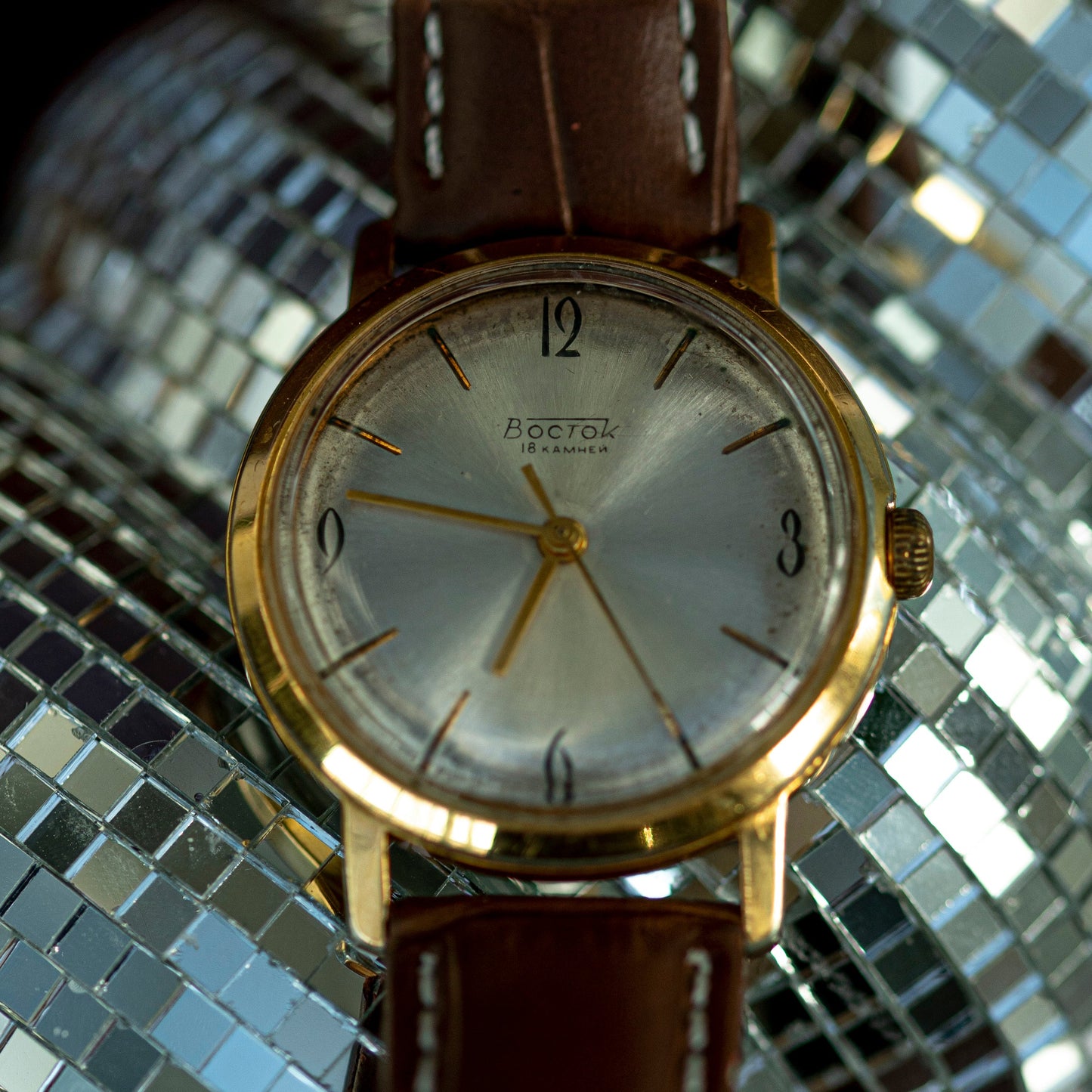 Vintage watch with a brown leather strap on a reflective silver surface