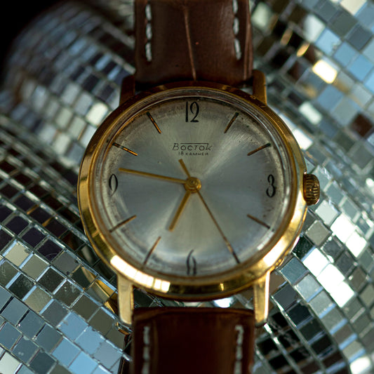 Vintage watch with a brown leather strap on a reflective silver surface