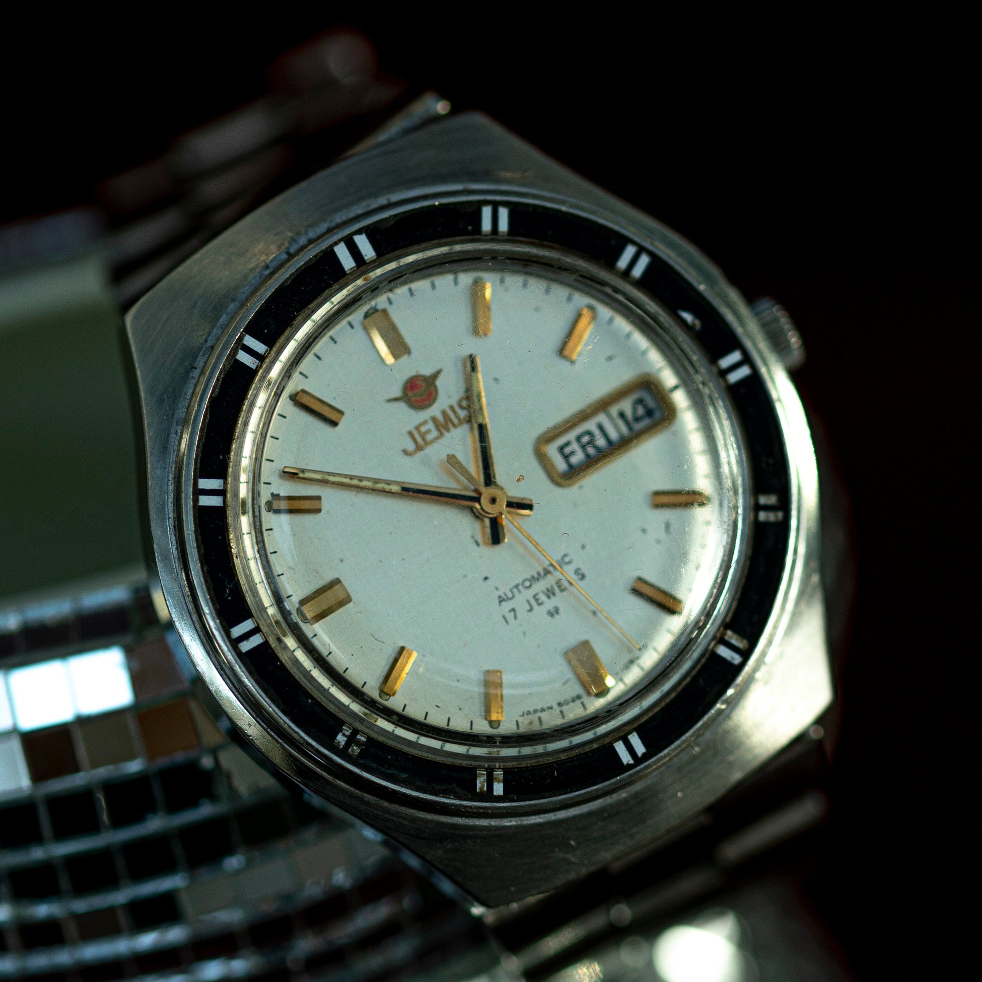 Vintage wristwatch with a white face and metallic band on a reflective surface.