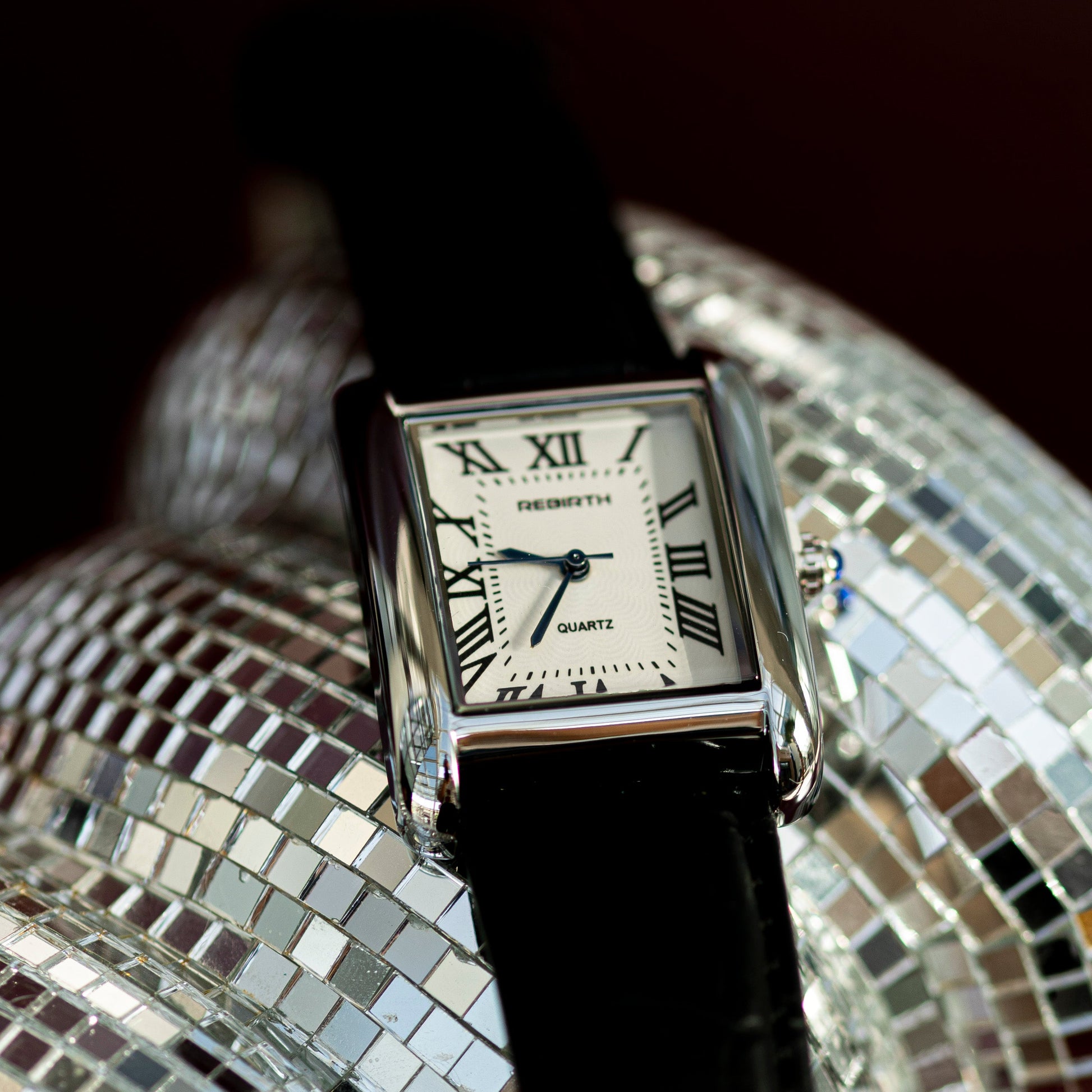 Watch with a black strap and square face featuring Roman numerals on a decorative background.