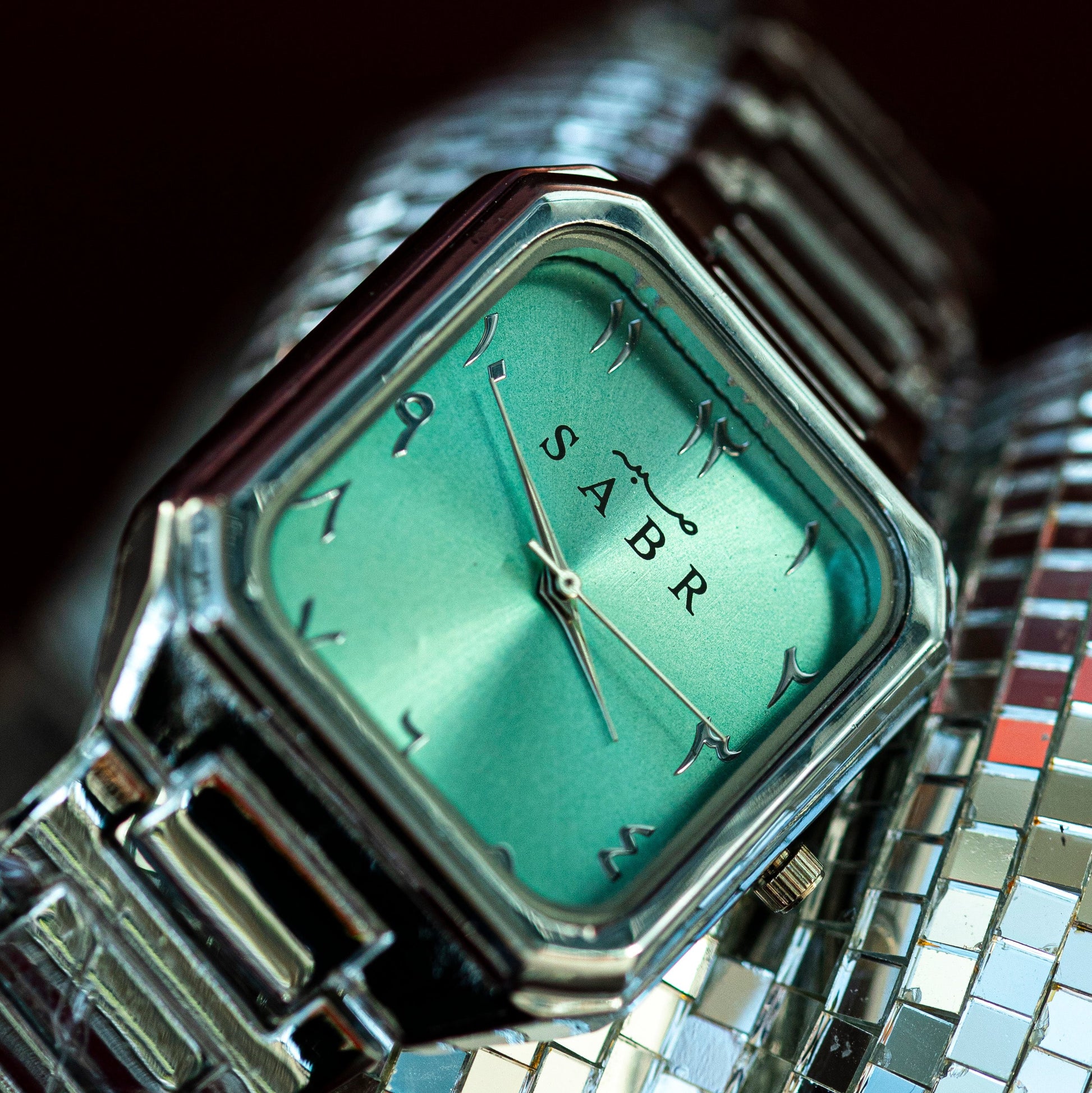 Watch with a green face and 'SABR' branding on a reflective surface
