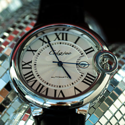Watch with a silver case and black strap on a reflective surface
