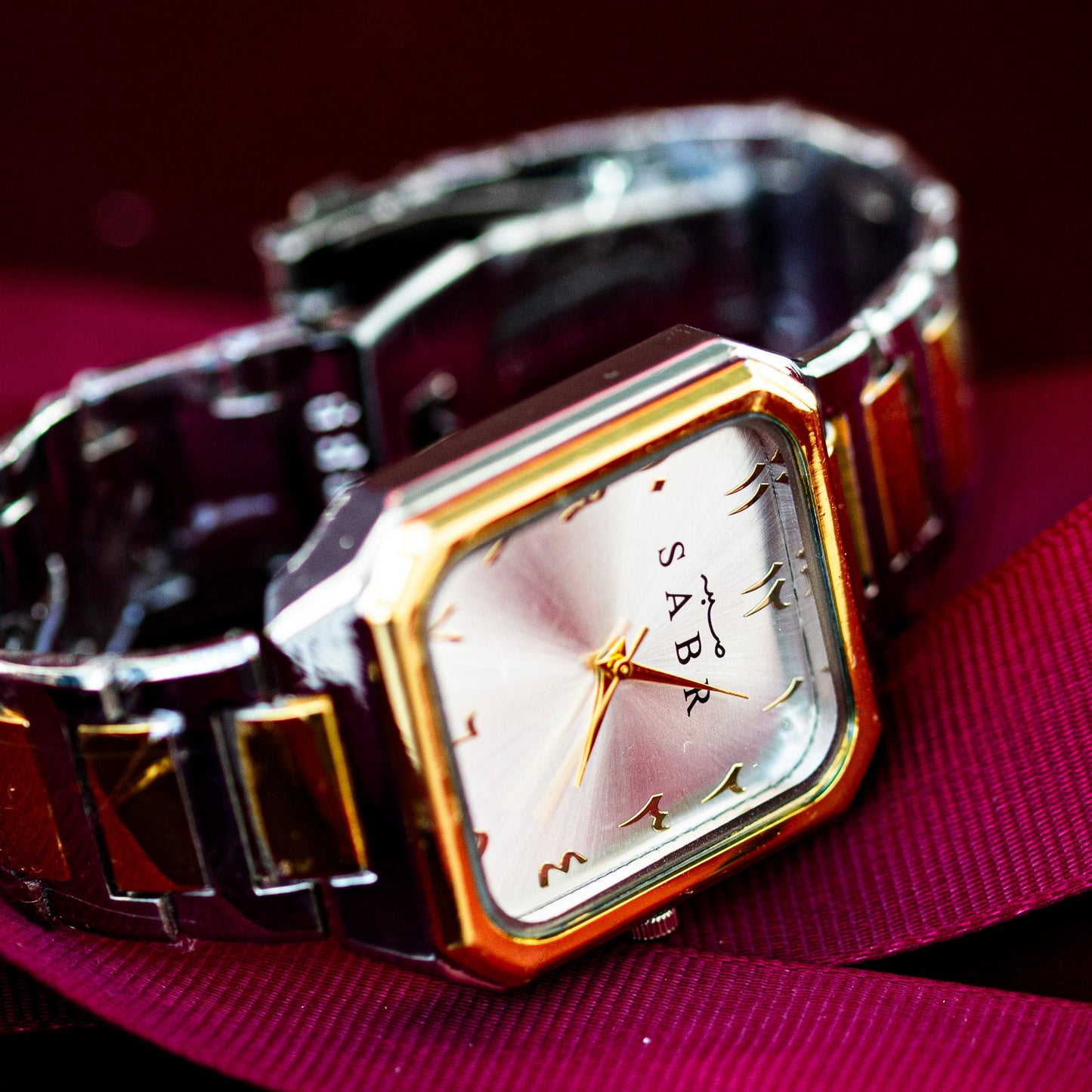 Wristwatch with a gold and silver band on a pink surface
