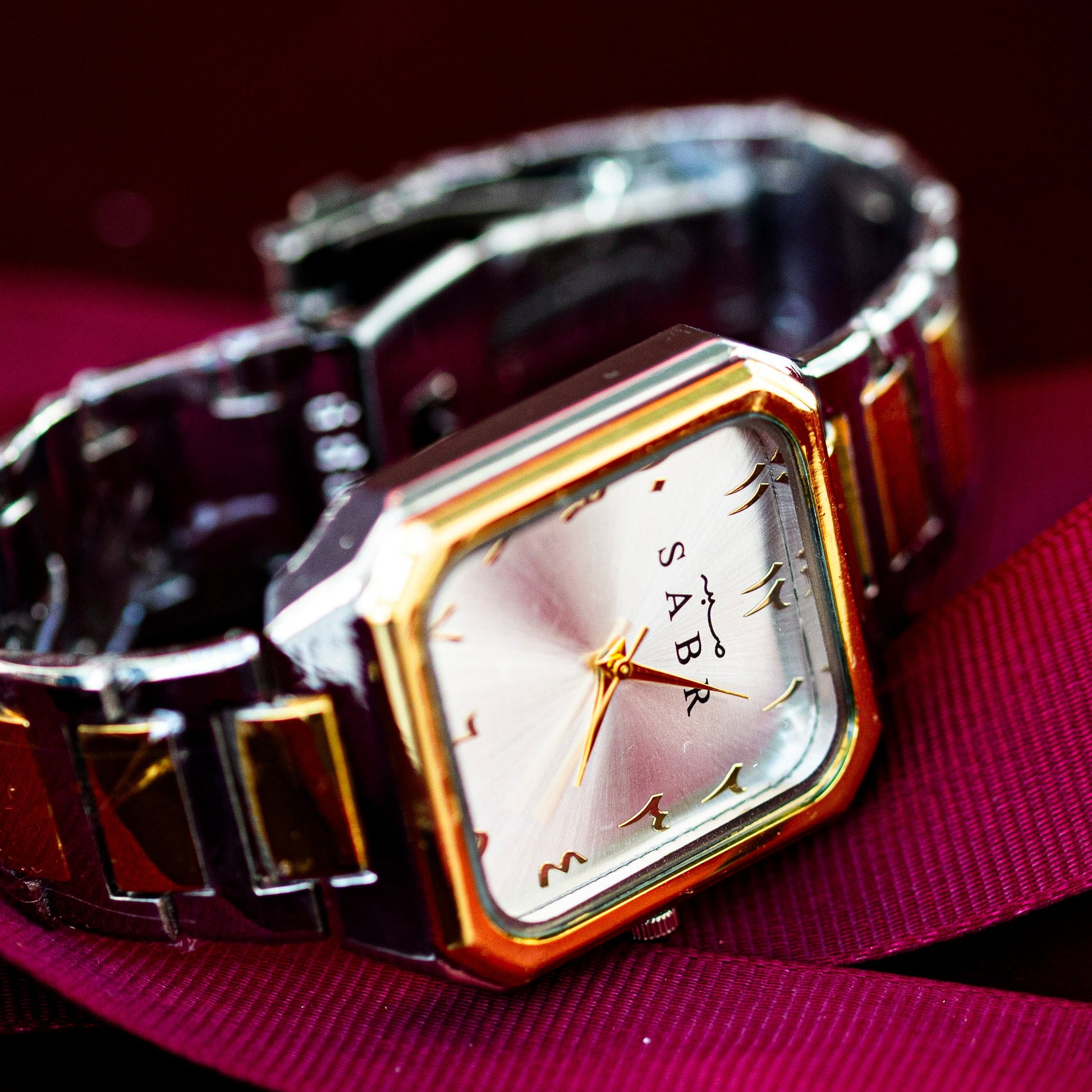 Wristwatch with a gold and silver band on a pink surface