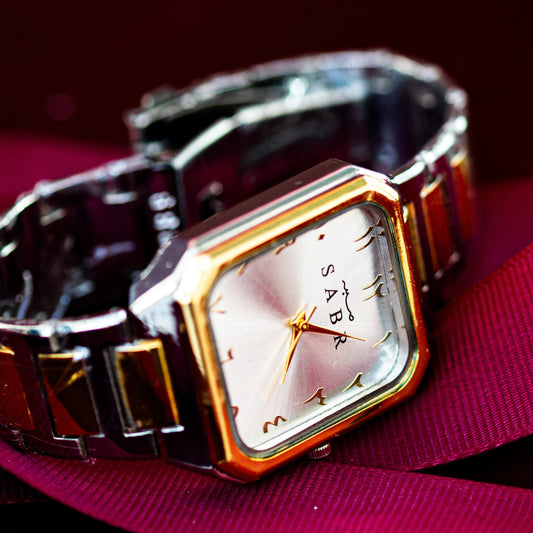 Wristwatch with a gold and silver band on a pink surface