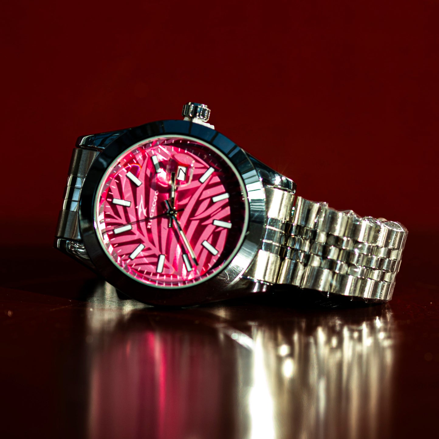 Wristwatch with pink face and silver metal strap on a reflective surface